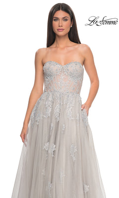 A woman stands against a plain white background wearing the La Femme Strapless Long A-Line Prom Dress 32111, featuring intricate embroidered-lace appliques and a sheer bodice.