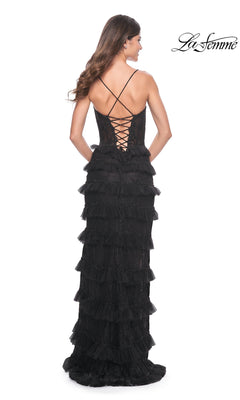 A woman models the La Femme Long Black Ruffled Prom Dress 32113 with thin straps and a lace-up back, standing against a white background. The "La Femme" logo appears in the top right corner.