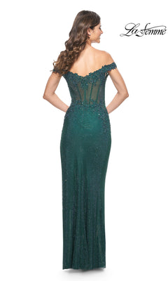 A woman wears the La Femme Off-Shoulder Long Corset Prom Dress 32116 in emerald green, featuring a fitted silhouette, beaded details, floor-length skirt, and a sheer corset bodice with her back to the camera.