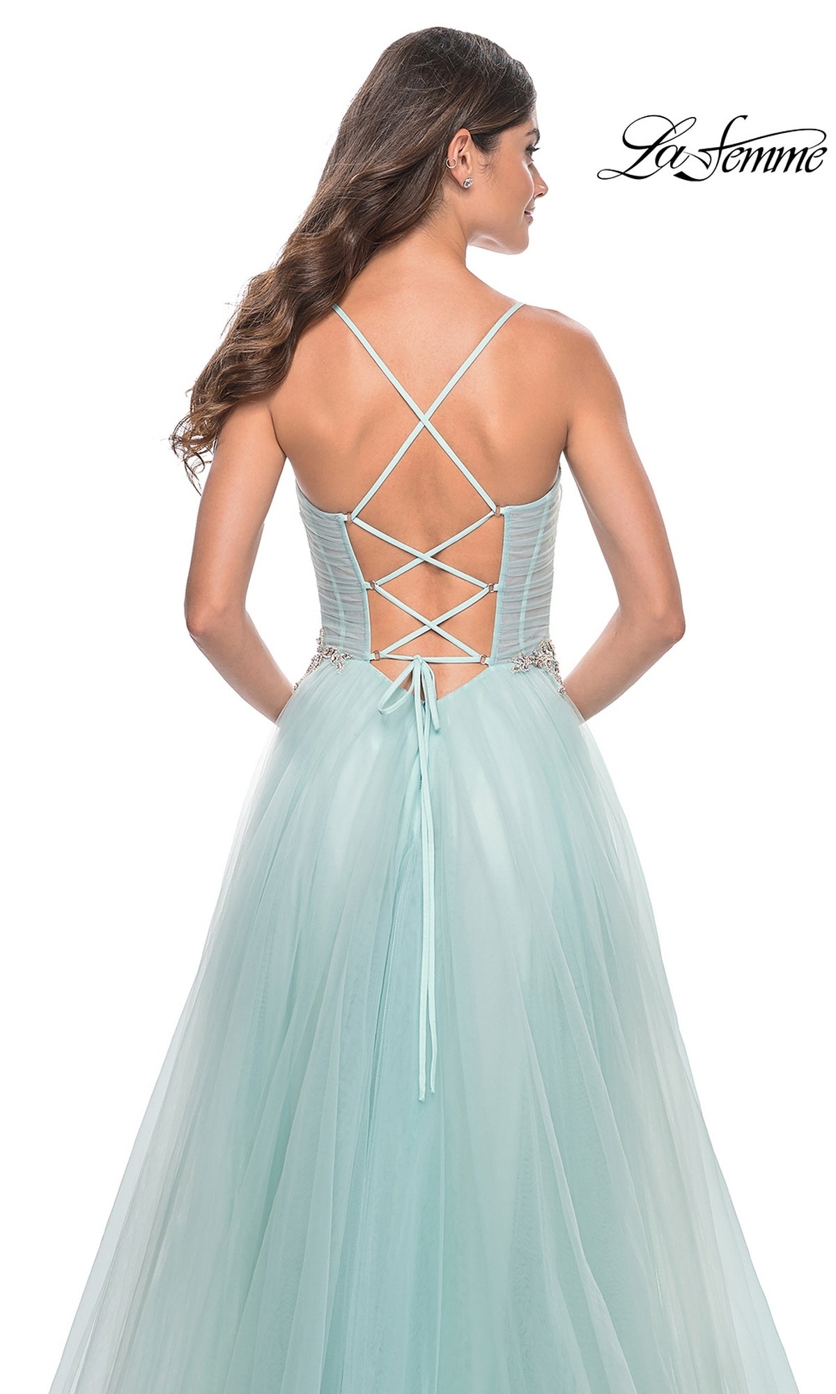 Woman in a light blue La Femme Sheer-Bodice Long A-Line Prom Dress 32117 with a lace-up corset back and crossed shoulder straps, standing away from the camera. 