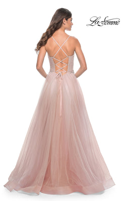 A woman stands facing away in the La Femme Sheer-Bodice Long A-Line Prom Dress 32117, featuring blush pink fabric, a lace-up corset back, and crisscross straps.