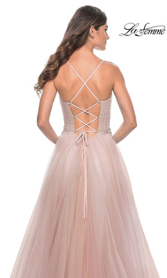Woman in a blush pink La Femme Sheer-Bodice Long A-Line Prom Dress 32117 with strappy open-back, thin crisscross straps, tulle skirt, and beaded waist detail, standing with her back to the camera.