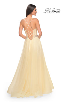 A woman models the La Femme Sheer-Bodice Long A-Line Prom Dress 32117 in light yellow, featuring an open back with crisscross lace-up details, against a plain white background.