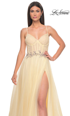 A woman in a light yellow La Femme Sheer-Bodice Long A-Line Prom Dress 32117 with thin straps, floral waist embellishments, and a high slit stands against a white background. The "La Femme" logo appears in the top right corner.