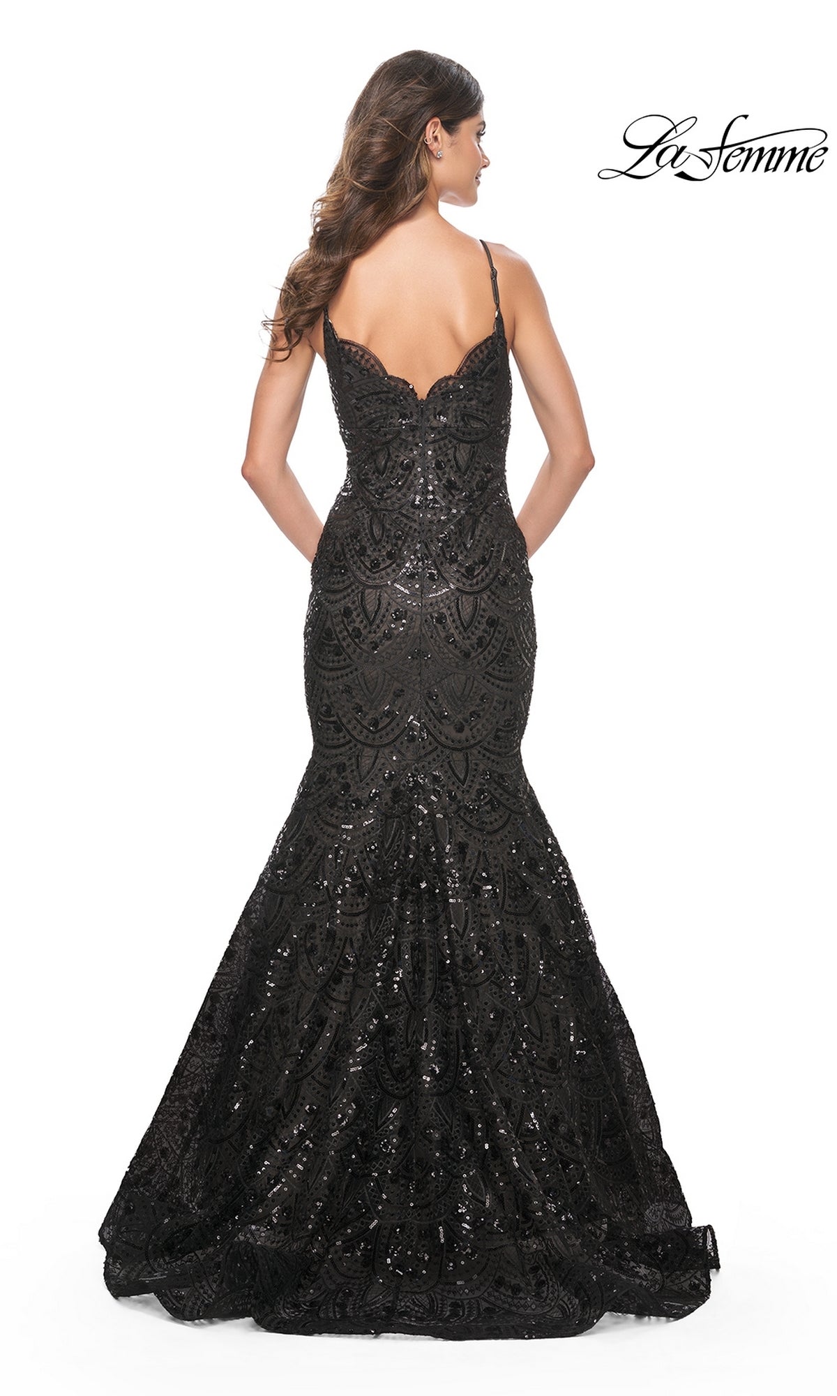 A woman faces away from the camera in the La Femme Black Sequin-Print Long Prom Dress 32118, featuring thin straps and a flared mermaid skirt. The fitted, floor-length dress dazzles against the white background.