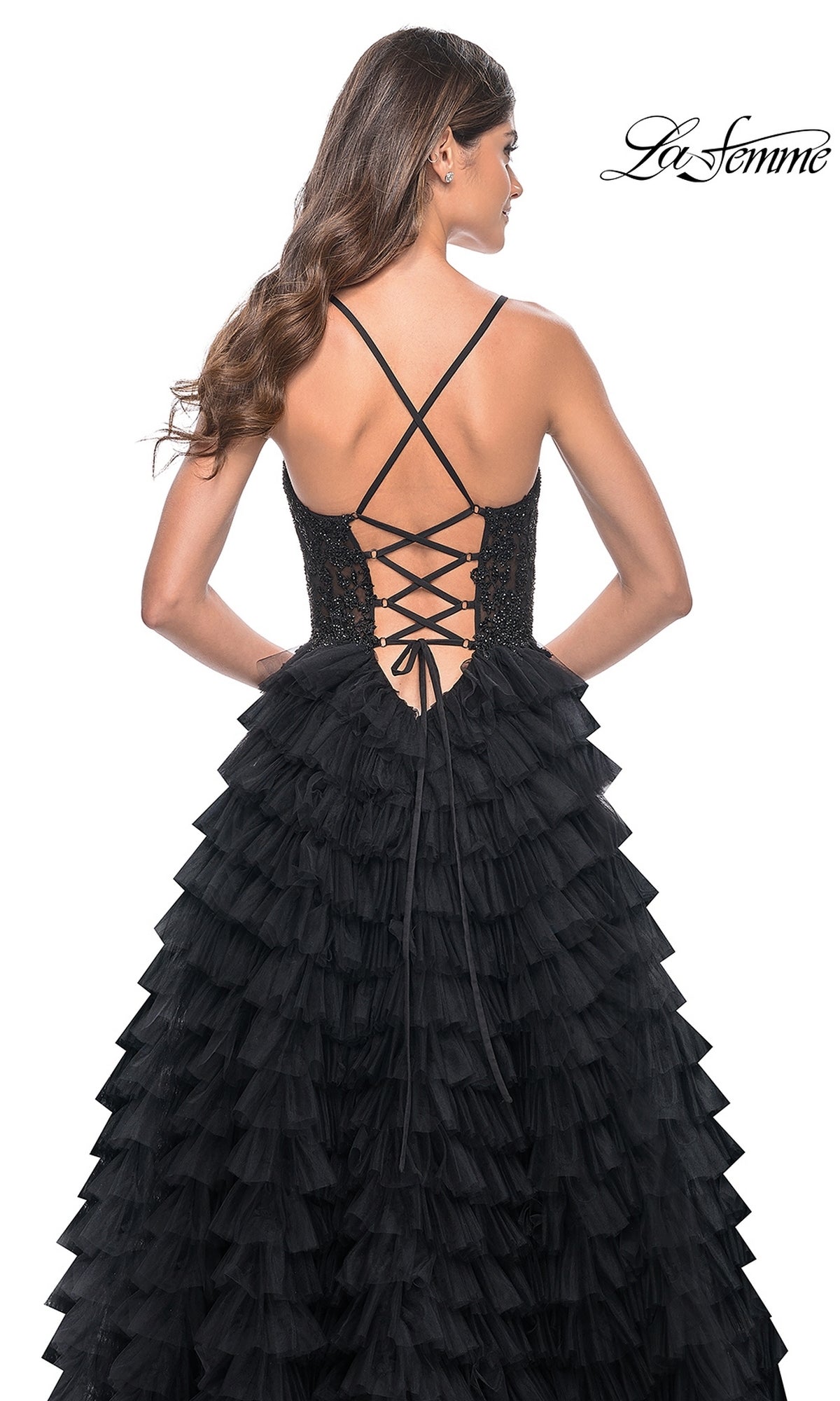 Woman in the La Femme Long Ruffled Prom Ball Gown 32128—a black tiered formal dress with lace-up corset back and crisscross straps—standing against a white background.