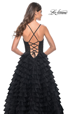 Woman in the La Femme Long Ruffled Prom Ball Gown 32128—a black tiered formal dress with lace-up corset back and crisscross straps—standing against a white background.