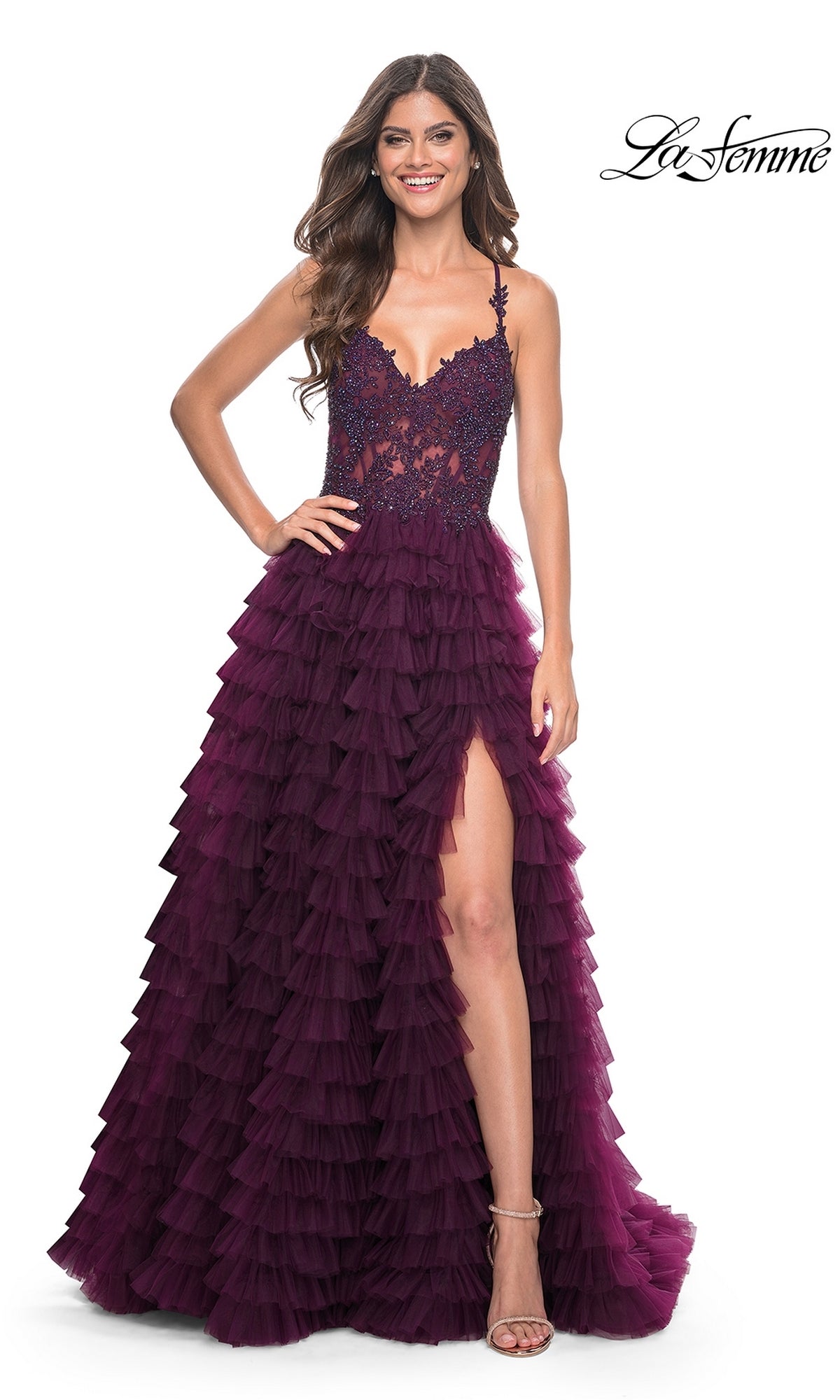 A woman poses in the La Femme Long Ruffled Prom Ball Gown 32128, a sleeveless deep purple dress with a high slit and lace bodice, against a white background.