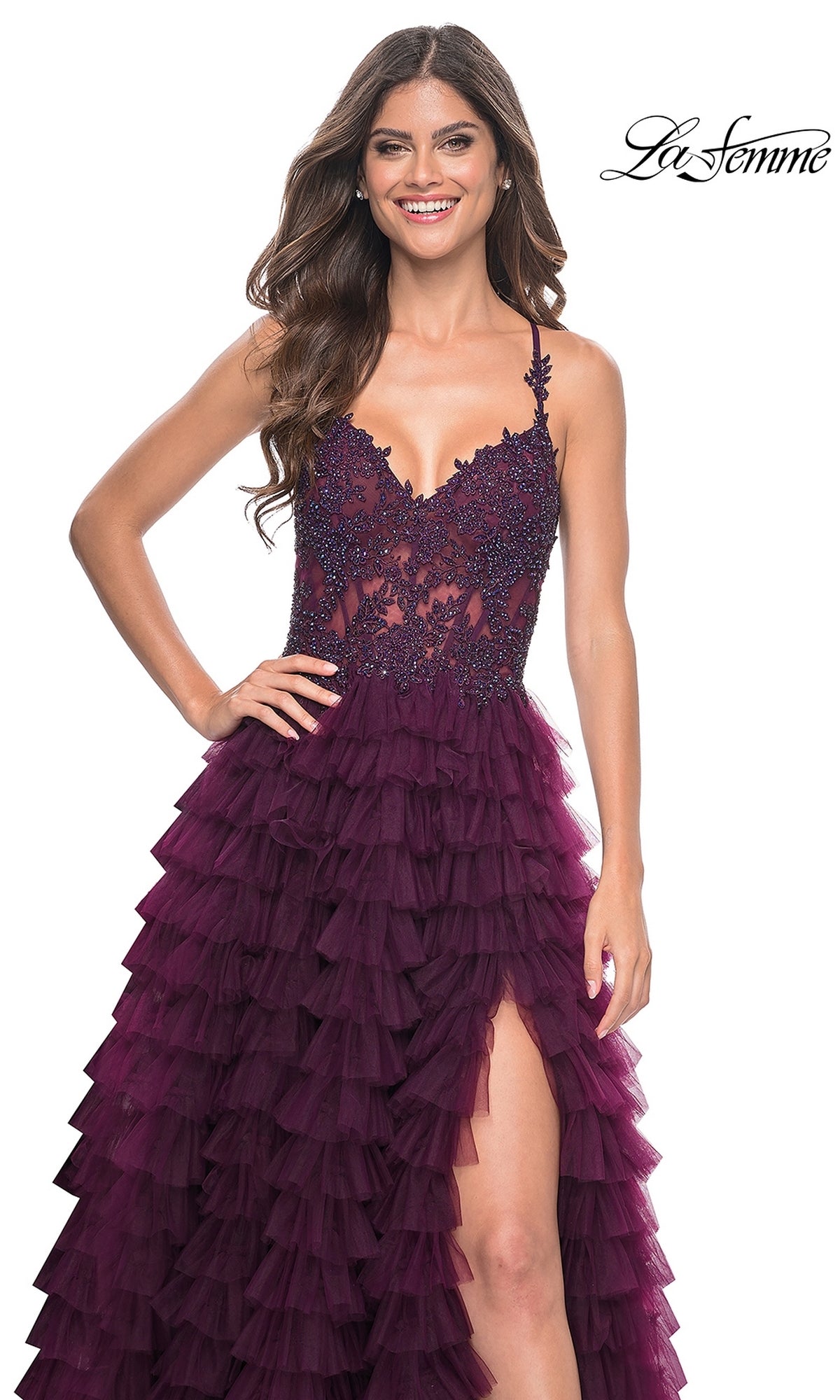 A woman stands and smiles against a white background, wearing the La Femme Long Ruffled Prom Ball Gown 32128—a sleeveless deep purple dress with a lace bodice, high slit, and long ruffled skirt.