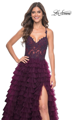 A woman stands and smiles against a white background, wearing the La Femme Long Ruffled Prom Ball Gown 32128—a sleeveless deep purple dress with a lace bodice, high slit, and long ruffled skirt.