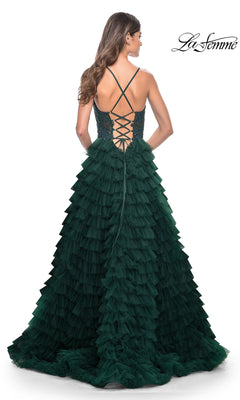 Woman in the La Femme Long Ruffled Prom Ball Gown 32128—floor-length, dark green with a voluminous tiered skirt and lace-up open back—stands facing away from the camera.