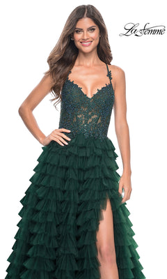 A woman stands smiling in the La Femme Long Ruffled Prom Ball Gown 32128, featuring a dark green hue, sheer beaded bodice, and spaghetti straps. The "La Femme" logo appears in the top right corner.