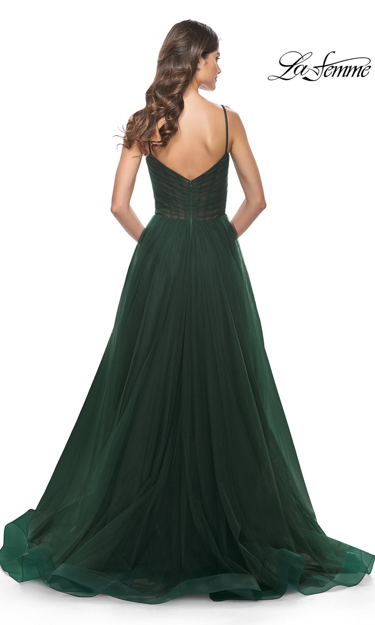 Woman in a La Femme Sheer-Waist Long A-Line Prom Dress 32130, emerald green with tulle skirt and thin straps, shown from the back against a white background.