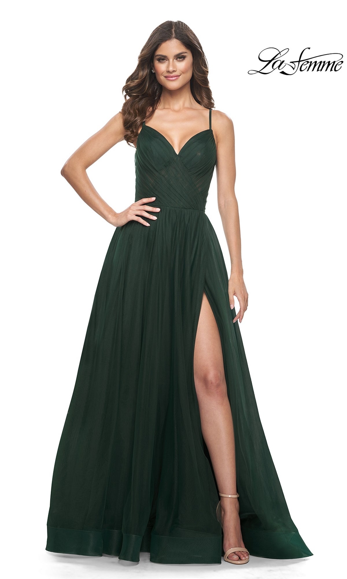 Woman in the La Femme Sheer-Waist Long A-Line Prom Dress 32130, dark green with thin straps, thigh-high slit, and fitted bodice, posing elegantly with one hand on her hip.