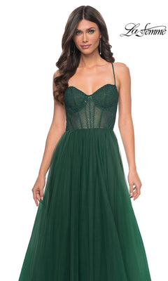 A woman wears the La Femme Embellished Long Tulle Prom Dress 32135, featuring a dark green mesh beaded bodice and a flowing A-line skirt, standing against a white background.