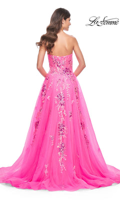 A woman with long brown hair models the La Femme Neon Pink Long Prom Ball Gown 32137, a strapless dress with sequin floral embroidery, standing with her back to the camera. The La Femme logo appears in the upper right corner.