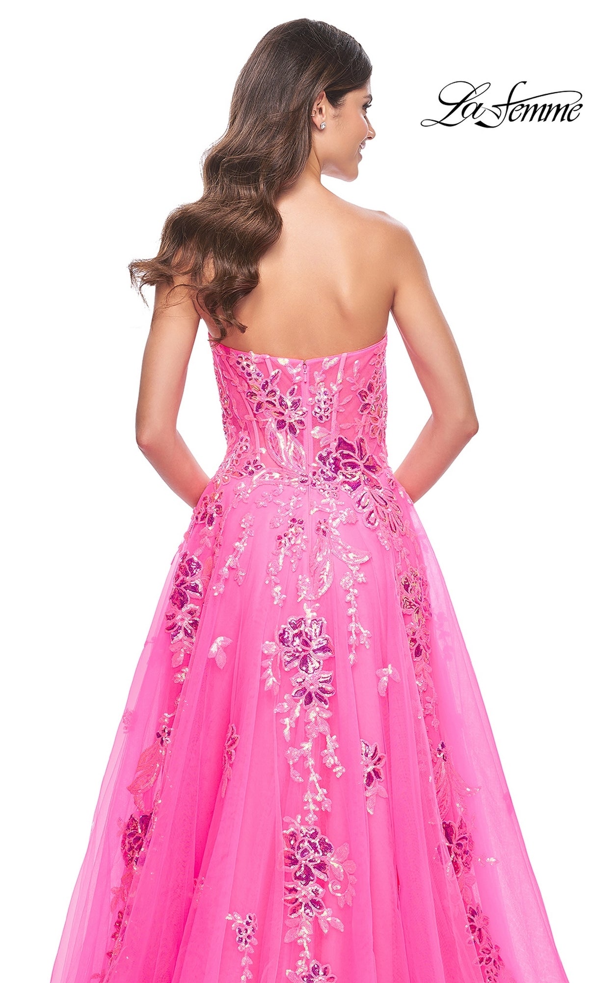 A woman with long wavy hair is seen from the back wearing the La Femme Neon Pink Long Prom Ball Gown 32137, a strapless dress featuring floral and sequin embellishments. The La Femme logo appears in the top right corner.