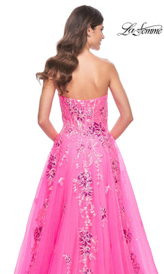 A woman with long wavy hair is seen from the back wearing the La Femme Neon Pink Long Prom Ball Gown 32137, a strapless dress featuring floral and sequin embellishments. The La Femme logo appears in the top right corner.