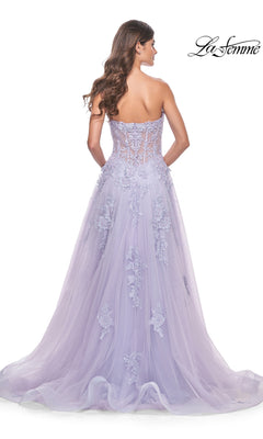 Wearing the La Femme Strapless Long Lace Prom Dress 32145, a woman stands facing away. The formal A-line gown features embroidered floral lace appliqué, a sheer bodice, a flowing full skirt, and an elegant long train.