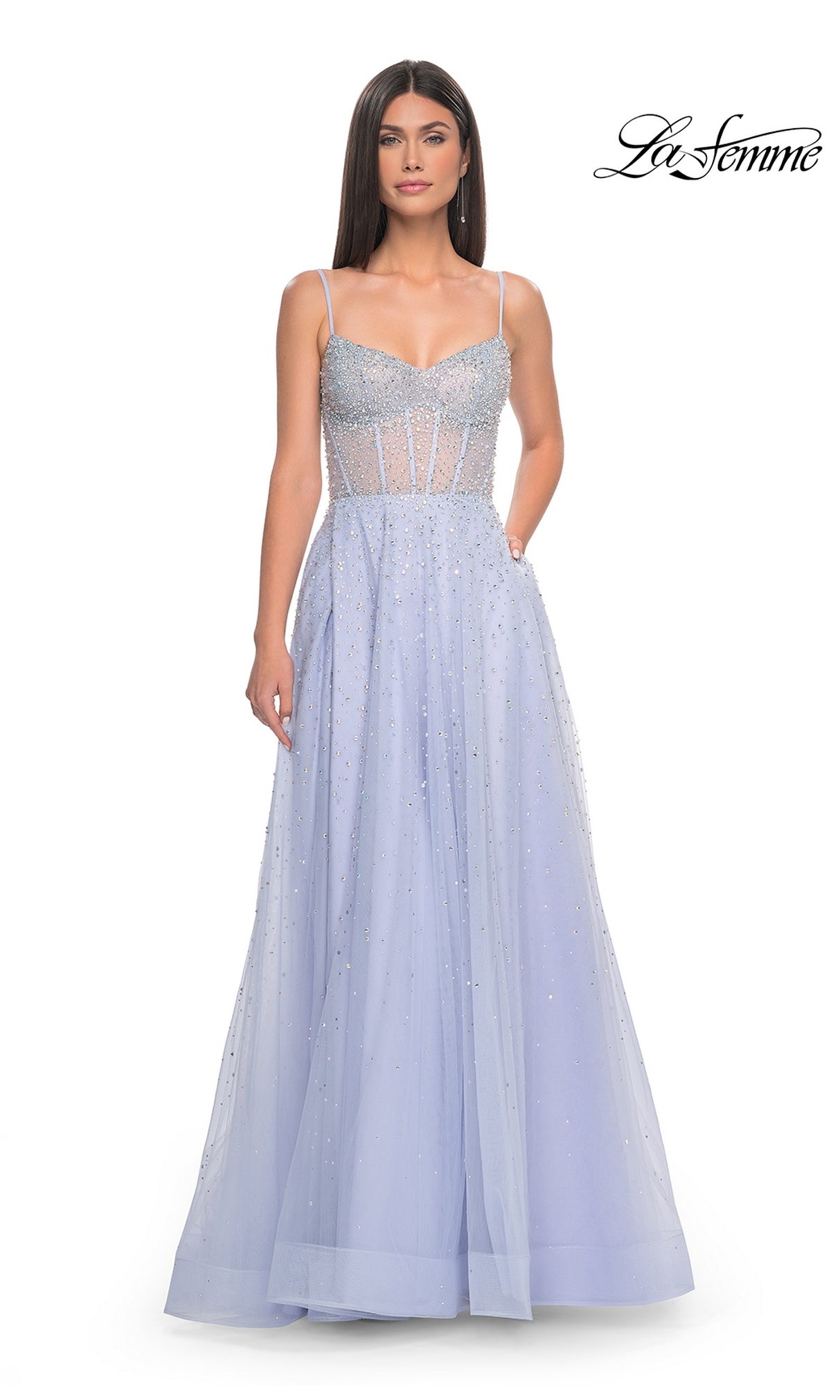 A woman wears the La Femme Beaded Long A-Line Prom Dress 32146 in light blue, featuring thin straps, a sheer bodice, and a floor-length skirt, as she stands against a white background.
