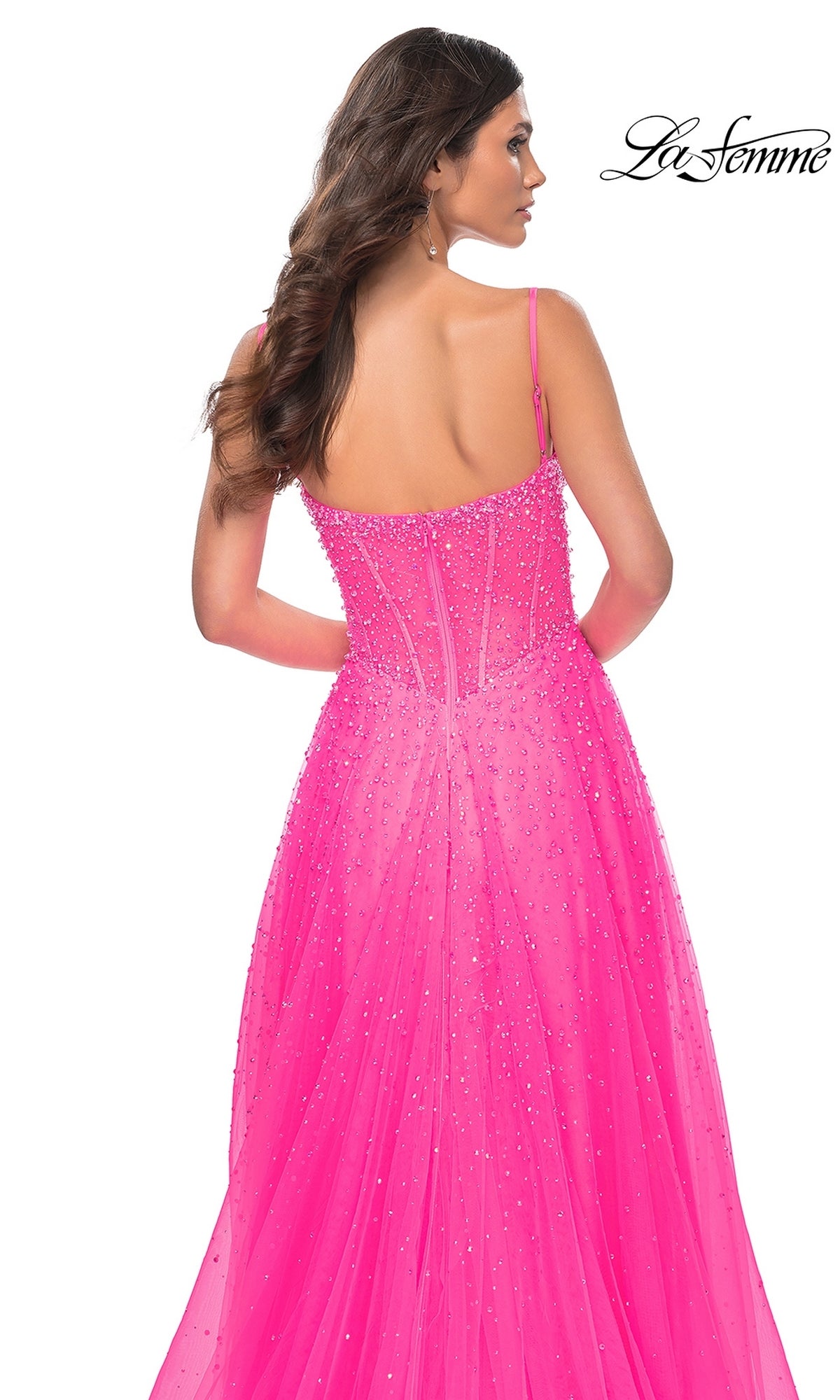 A woman is shown from behind wearing the La Femme Beaded Long A-Line Prom Dress 32146 in bright pink, featuring thin straps and a semi-sheer back, against a white background with the 