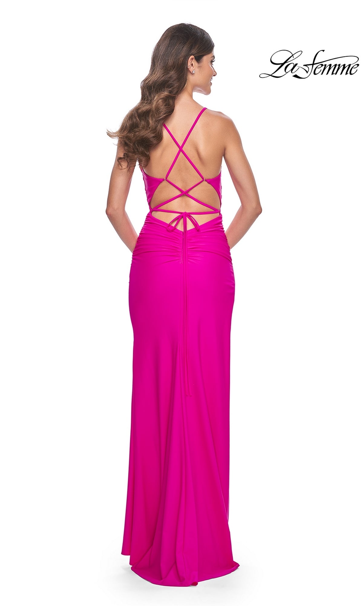 A woman, seen from the back, wears the La Femme Strappy-Back Long Jersey Prom Dress 32152 in bright pink, featuring a strappy open-back design. The 