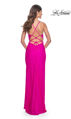 A woman, seen from the back, wears the La Femme Strappy-Back Long Jersey Prom Dress 32152 in bright pink, featuring a strappy open-back design. The "La Femme" logo appears in the top right corner of the image.