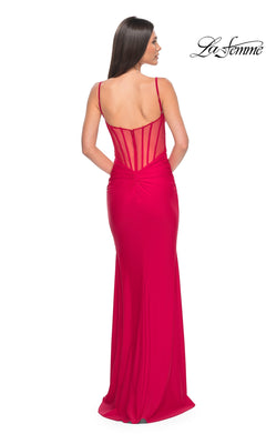 A woman wears the La Femme Sheer-Back Long Jersey Prom Dress 32153, a floor-length red gown with spaghetti straps and a sheer corset-style back, standing against a white background.