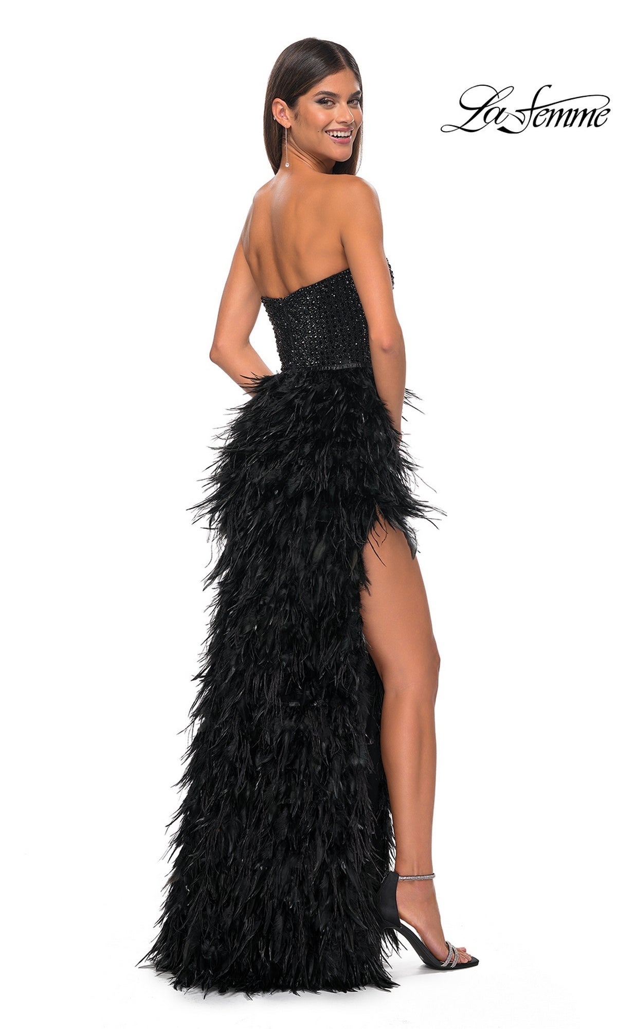 A woman in the La Femme Feather Strapless Long Prom Dress 32165, featuring an embellished sweetheart bodice and feathered skirt, stands in high heels smiling over her shoulder. The La Femme logo appears in the top right corner.
