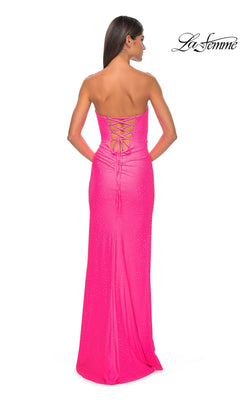 A woman stands facing away in the La Femme Twist Strapless Long Prom Dress 32175—a bright pink, floor-length gown with a lace-up back, fitted silhouette, and subtle sparkling embellishments.