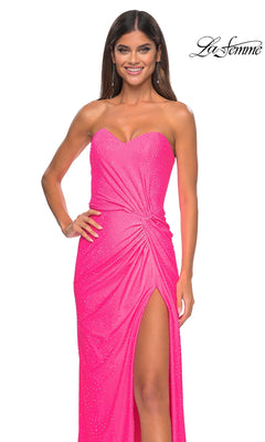 A woman models the La Femme Twist Strapless Long Prom Dress 32175, a bright pink beaded gown with a thigh-high slit and subtle embellishments, standing against a white background to showcase its elegant formal style.
