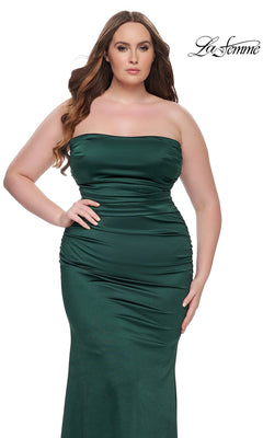 A woman poses against a white background in the La Femme Plus-Size Long Tube Prom Dress 32194, a strapless, fitted dark green gown that highlights her silhouette. The La Femme logo is displayed in the top right corner.