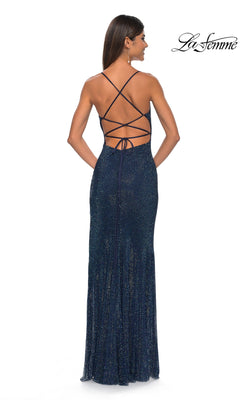 A woman wears the La Femme Embellished Long Fishnet Prom Dress 32203 in navy blue, featuring glitter details and an open criss-cross lace-up back, as she stands against a white background.