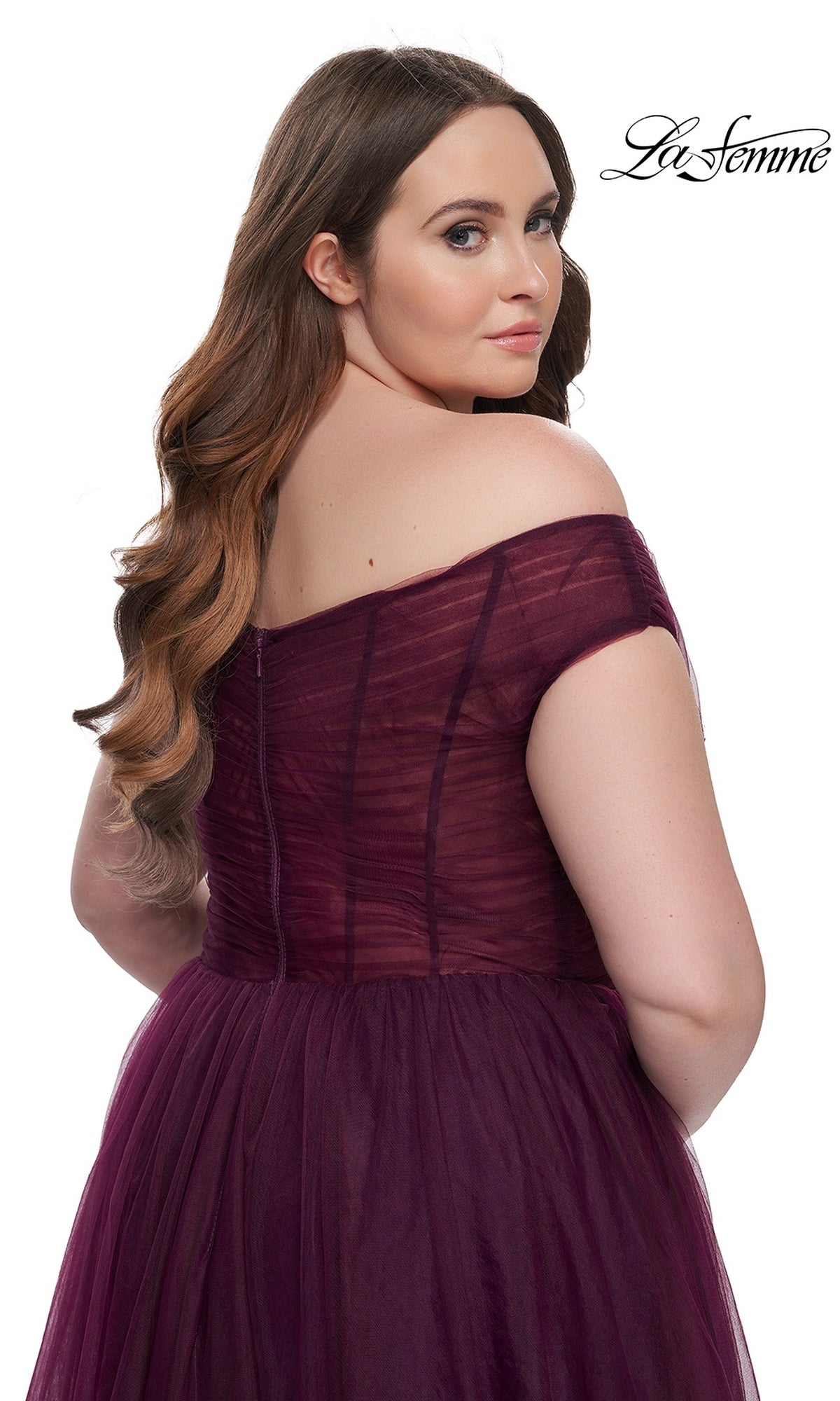 Plus-size model with long wavy hair in a burgundy off-the-shoulder La Femme A-line prom dress (style 32204), looking over her shoulder against a white background. 