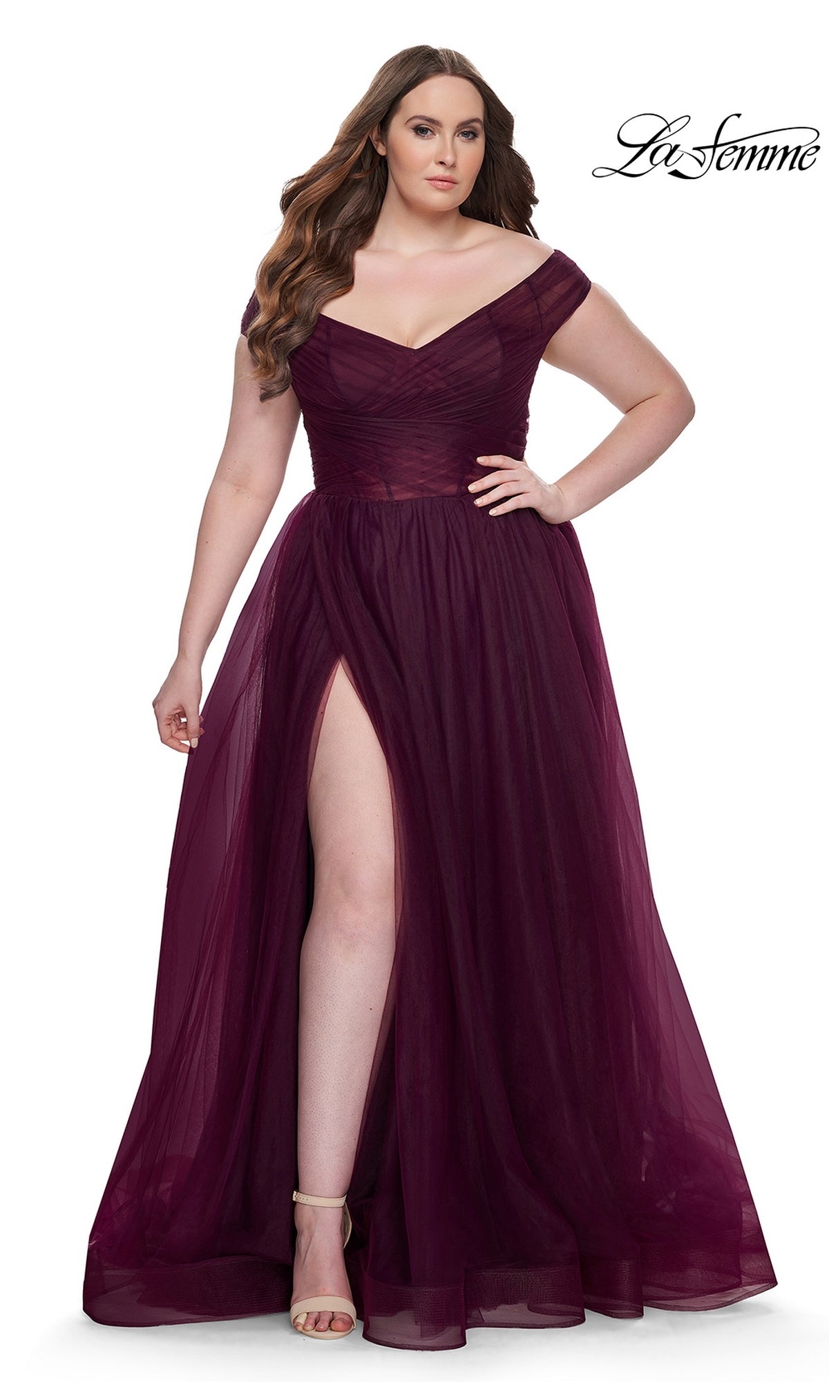 A woman models the La Femme Plus-Size Long A-Line Prom Dress 32204, featuring a deep burgundy hue, off-the-shoulder neckline, fitted bodice, flowing tulle skirt, and high leg slit against a white background.