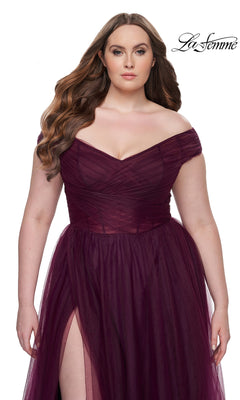 A woman models the La Femme Plus-Size Long A-Line Prom Dress 32204—an off-the-shoulder deep burgundy gown with tulle overlay and thigh-high slit—posing against a white background. "La Femme" appears in the top right corner.