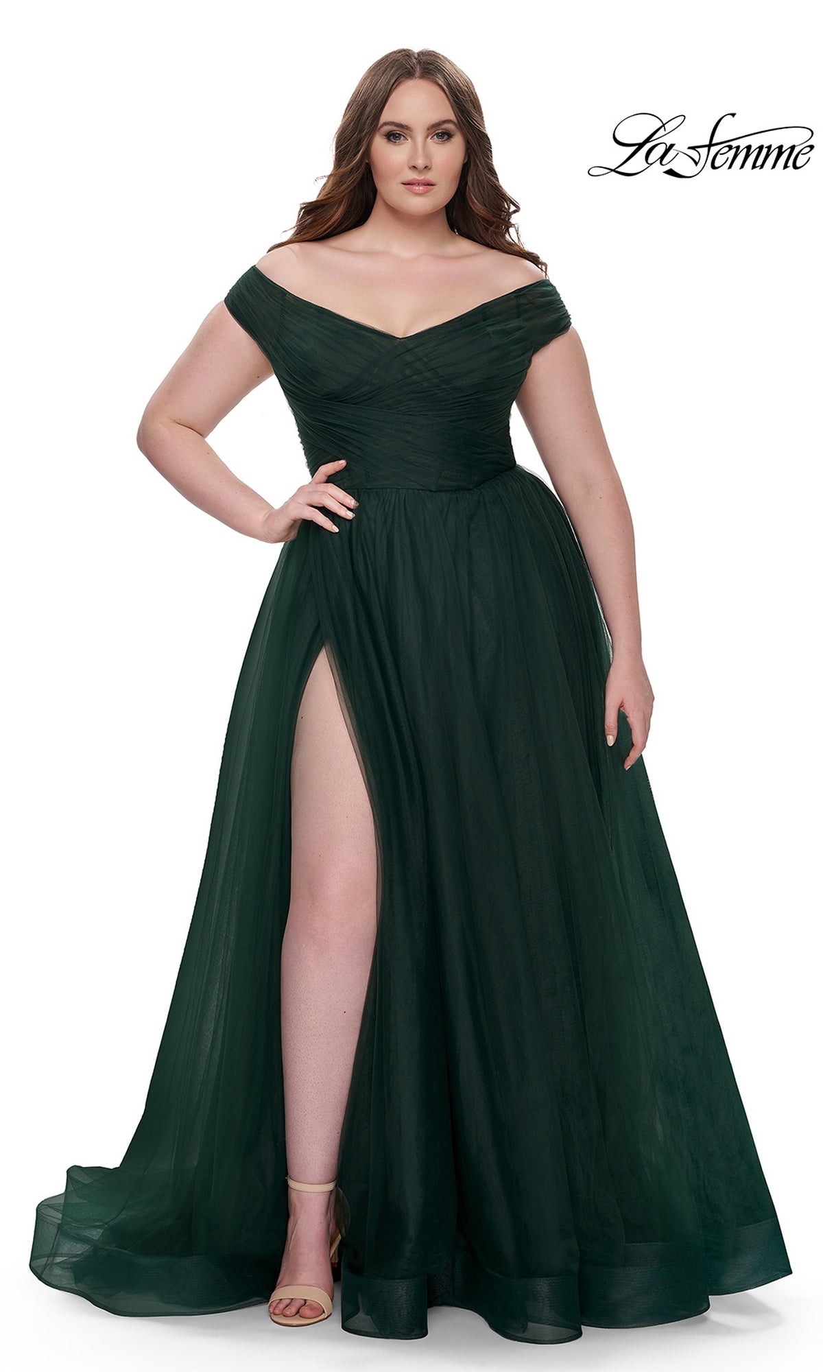 A woman models the La Femme Plus-Size Long A-Line Prom Dress 32204—a floor-length, off-the-shoulder dark green gown with a thigh-high slit and nude heels—against a white background. The La Femme logo appears in the top right corner.