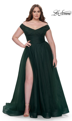 A woman models the La Femme Plus-Size Long A-Line Prom Dress 32204—a floor-length, off-the-shoulder dark green gown with a thigh-high slit and nude heels—against a white background. The La Femme logo appears in the top right corner.