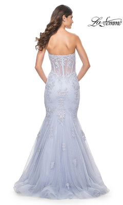 A woman wearing the La Femme Periwinkle Strapless Prom Dress 32214, featuring a fitted mermaid silhouette, sheer embroidered details, and a tulle train, viewed from the back.