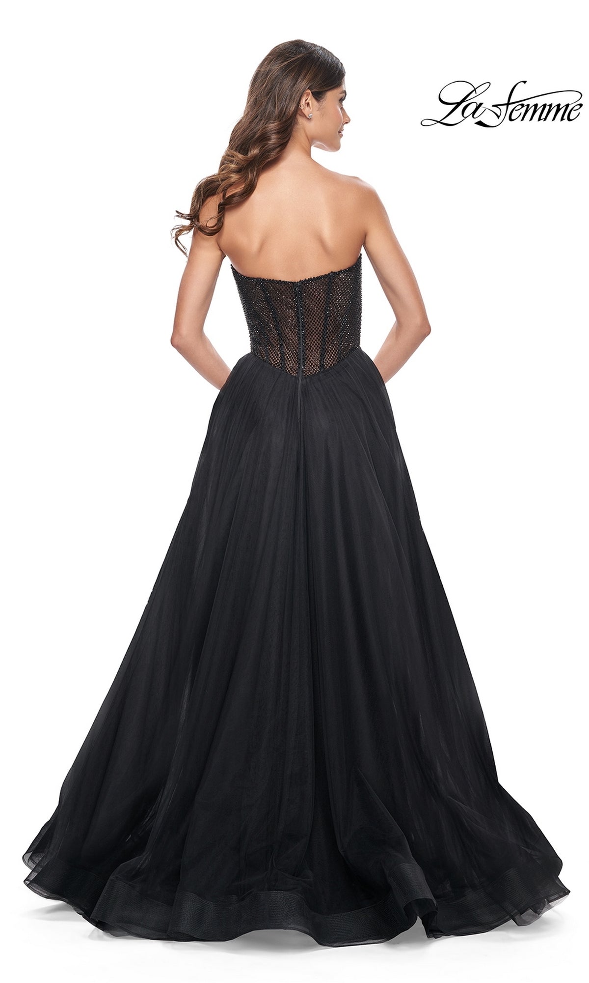 A woman stands with her back to the camera wearing the La Femme Strapless Long A-Line Prom Dress 32216 in black lace and tulle, featuring a fitted bodice and full skirt for an elegant formal look. The 