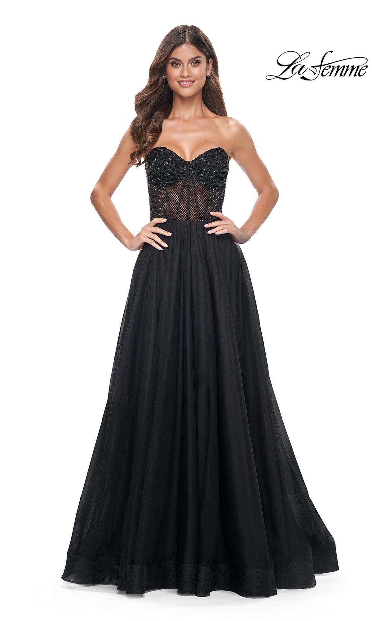 Woman in the La Femme Strapless Long A-Line Prom Dress 32216, featuring a beaded semi-sheer bodice and flowing skirt, stands with hands on hips. 