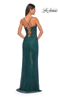 Woman in the La Femme Rhinestone Fishnet Long Prom Dress 32218—a floor-length, dark green sparkly gown with crisscross lace-up back—stands facing away from the camera. "La Femme" logo displayed in the upper right corner.