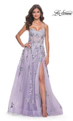 A woman models the La Femme Long Lavender A-Line Prom Dress 32221, featuring floral appliqué, a sheer bodice, thin straps, and a high side slit. She poses elegantly with one hand on her hip. The "La Femme" logo is displayed.