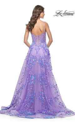 A woman in the La Femme Sequin-Print Long A-Line Prom Dress 32223, featuring a purple floral design with thin straps and a sheer back, stands facing away. The flowing train enhances the elegance. The La Femme logo appears in the upper right corner.