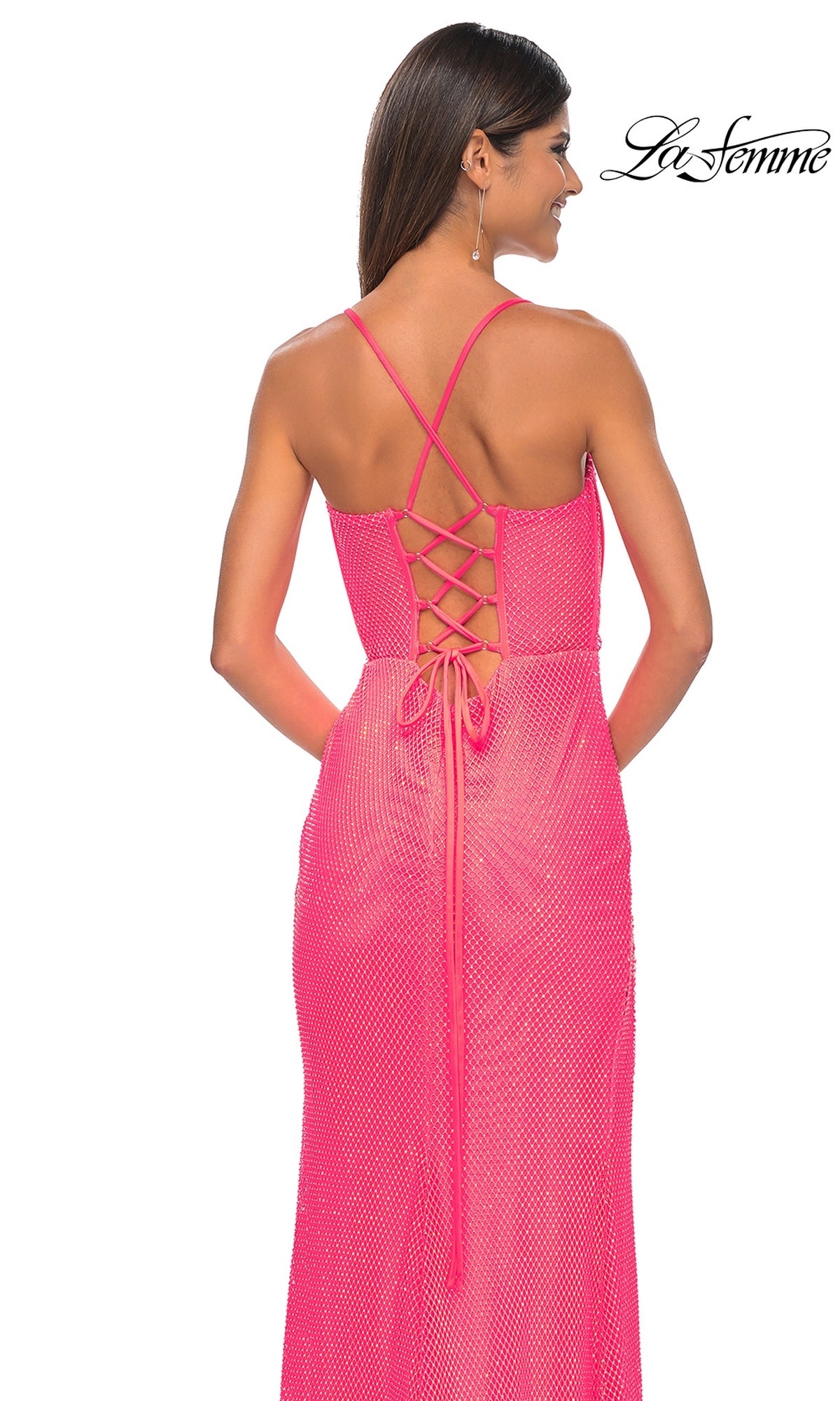 A woman stands with her back to the camera in a pink La Femme Sheer Bustier Long Prom Dress 32227, featuring a sleeveless design, lace-up back, thin crisscross straps, and a subtle textured pattern.