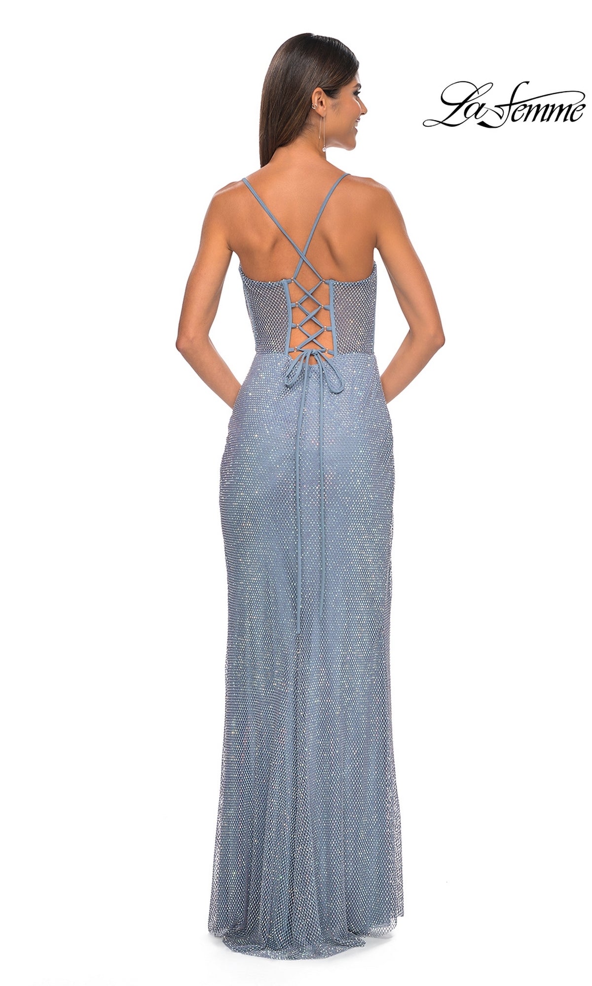 A woman stands facing away, wearing the La Femme Sheer Bustier Long Prom Dress 32227—a sparkly, light blue, floor-length gown with thin straps and a lace-up back.