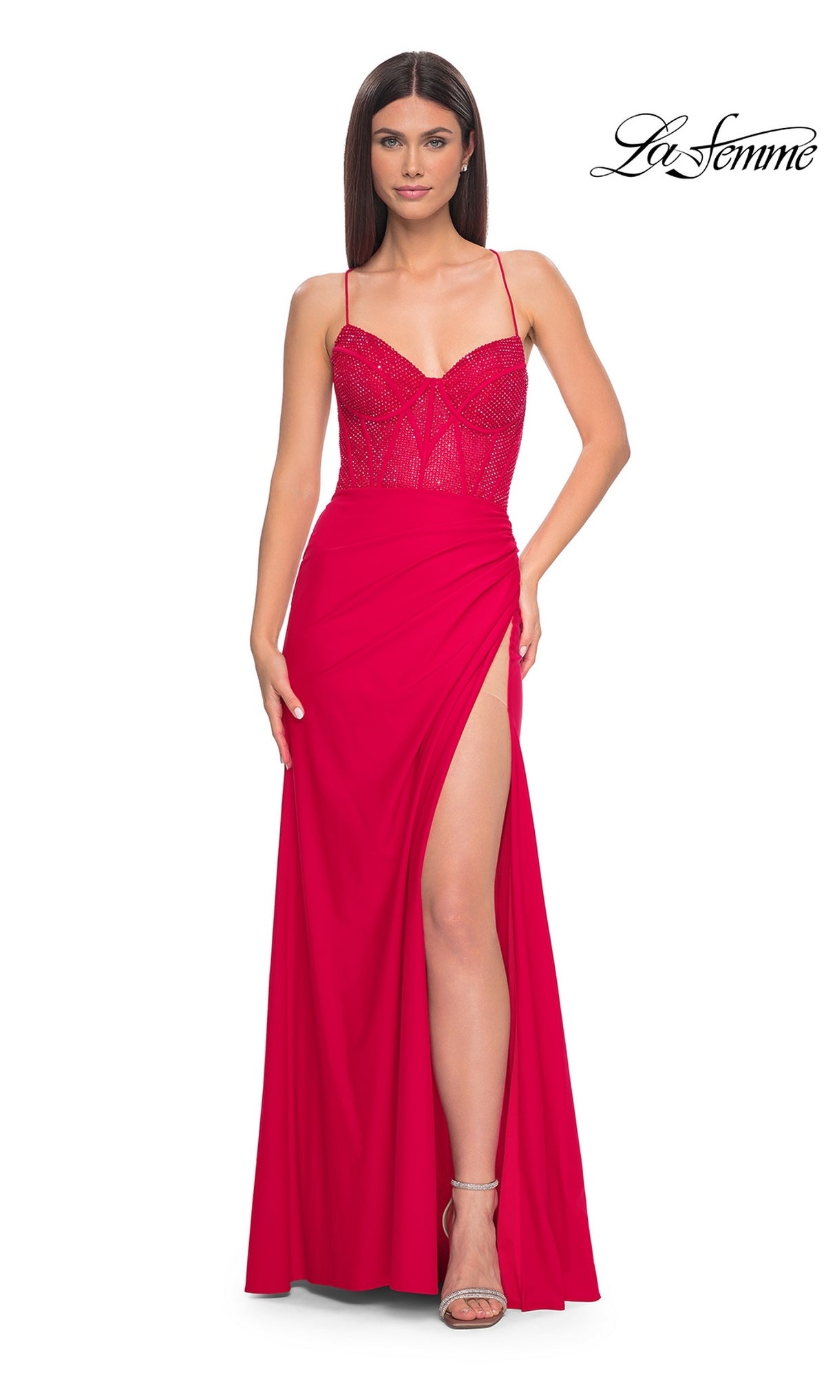 Woman in a red La Femme Lace-Up Long Fishnet Prom Dress 32230 featuring a beaded sheer corset bodice, spaghetti straps, and high side slit, paired with open-toe heels. White background with La Femme logo in the top right corner.