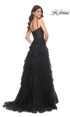 Woman in a La Femme Sheer-Waist Long Ruffled Prom Dress 32233, a black sleeveless gown with spaghetti straps and layered tulle, stands smiling over her shoulder against a white background.
