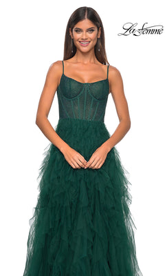 A woman stands smiling against a white background in the La Femme Sheer-Waist Long Ruffled Prom Dress 32233—a sleeveless, dark green gown with beaded details and a fitted corset bodice. The "La Femme" logo appears in the top right corner.