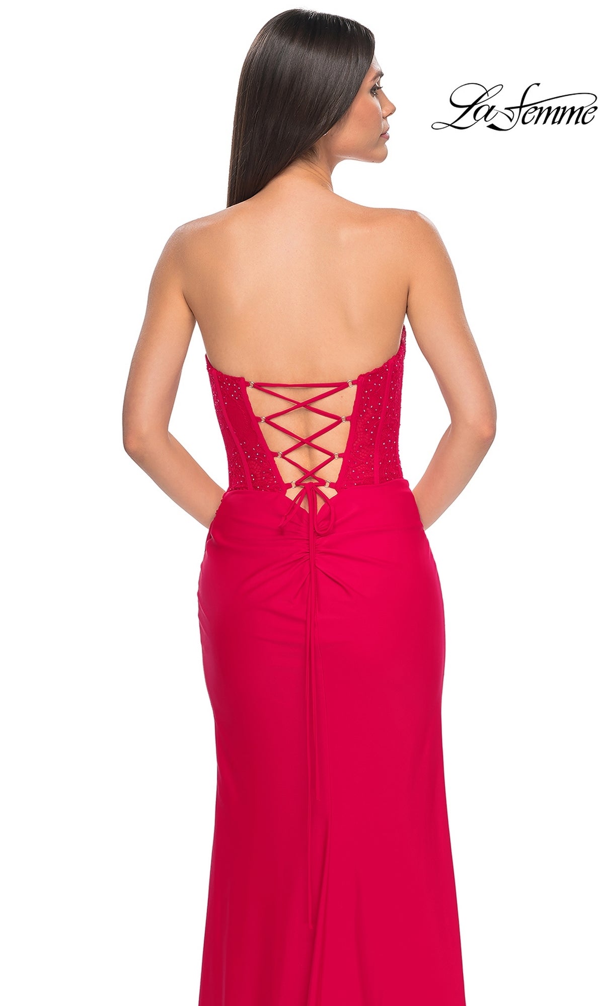 A woman stands facing away, wearing the La Femme Strapless Long Corset Prom Dress 32234 featuring a lace-up back. The 